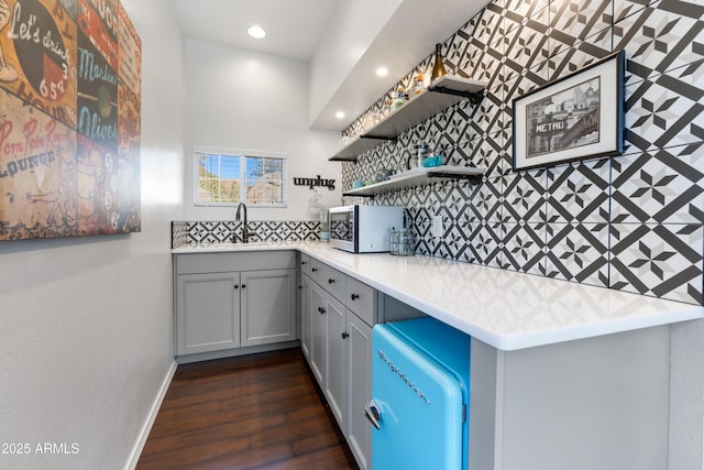 kitchen featuring tasteful backsplash, sink, gray cabinetry, dark hardwood / wood-style flooring, and kitchen peninsula