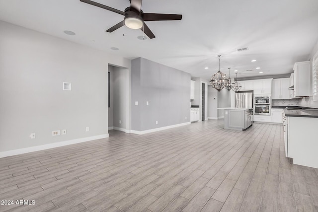 unfurnished living room featuring ceiling fan with notable chandelier and light hardwood / wood-style flooring