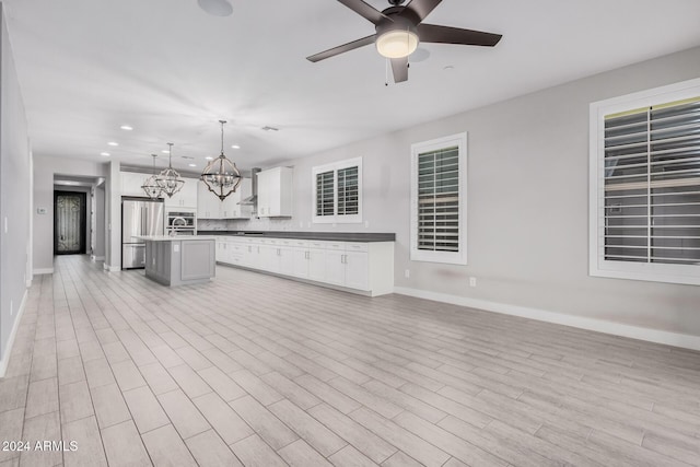 kitchen featuring pendant lighting, a center island with sink, white cabinets, wall chimney exhaust hood, and stainless steel refrigerator