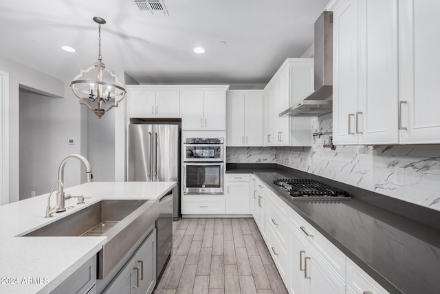 kitchen featuring white cabinetry, sink, stainless steel appliances, hanging light fixtures, and wall chimney range hood