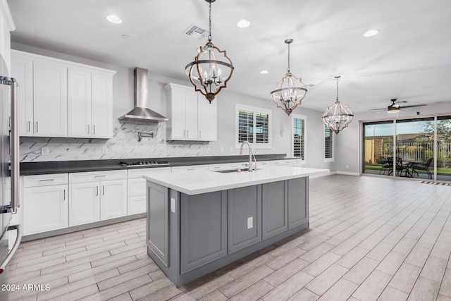 kitchen featuring ceiling fan with notable chandelier, decorative light fixtures, white cabinetry, and wall chimney range hood