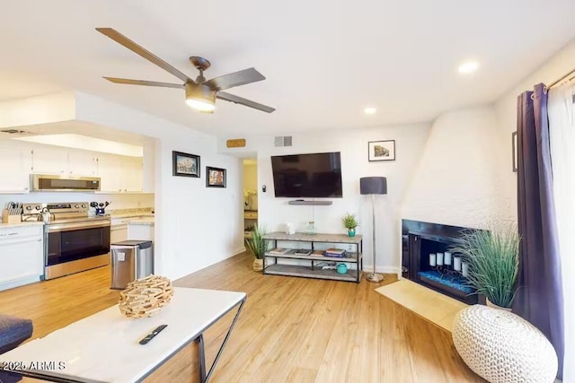 living room with ceiling fan, a fireplace with flush hearth, light wood-style flooring, and recessed lighting