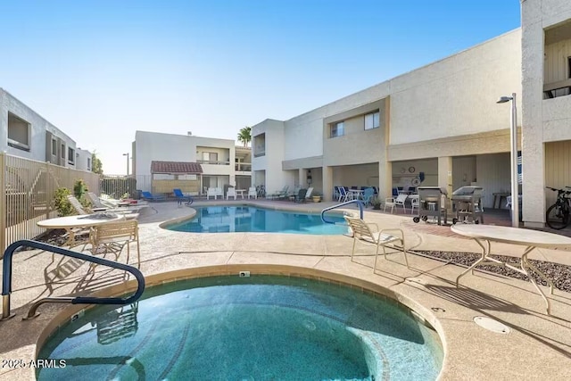 community pool with a hot tub, a patio area, and fence