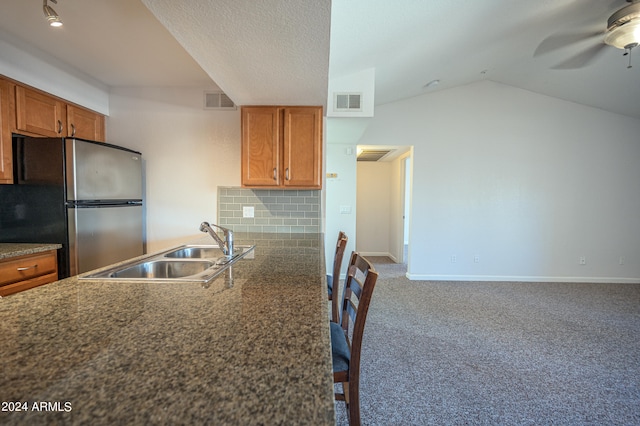 kitchen with backsplash, lofted ceiling, stainless steel refrigerator, carpet flooring, and sink