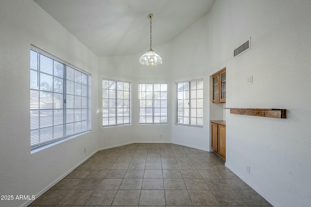 unfurnished dining area with light tile patterned floors, a towering ceiling, and a notable chandelier