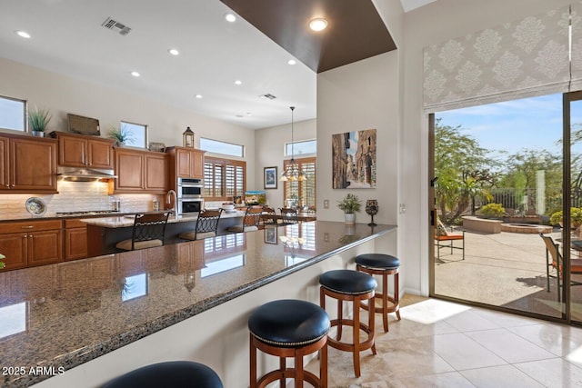 kitchen with a kitchen breakfast bar, tasteful backsplash, dark stone counters, pendant lighting, and appliances with stainless steel finishes