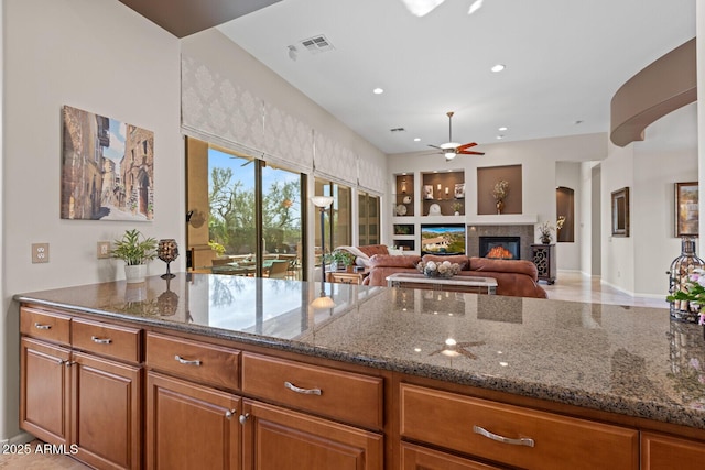 kitchen featuring ceiling fan, built in features, and dark stone counters