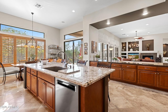 kitchen featuring light stone countertops, stainless steel dishwasher, sink, a center island with sink, and hanging light fixtures