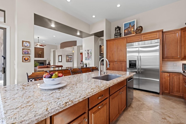 kitchen with appliances with stainless steel finishes, tasteful backsplash, light stone counters, ceiling fan, and sink