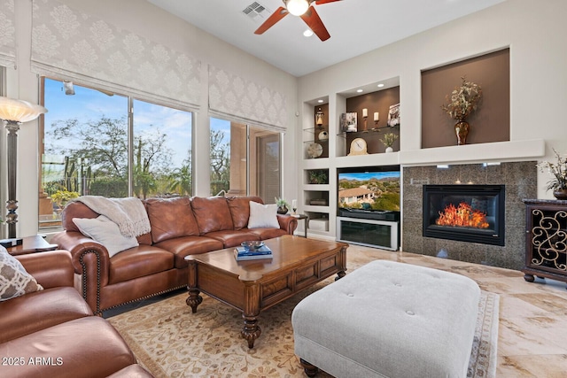 living room with built in shelves, ceiling fan, and a tiled fireplace