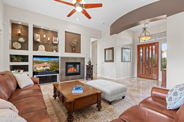 living room featuring a tile fireplace, built in shelves, and ceiling fan