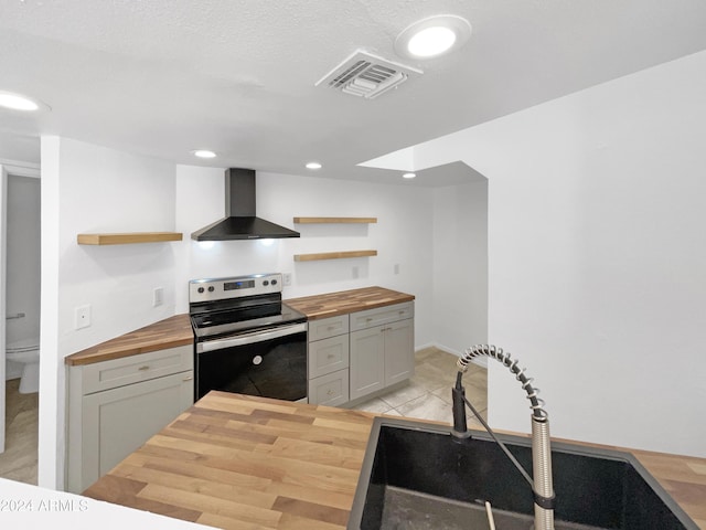 kitchen with butcher block counters, stainless steel electric range oven, sink, and wall chimney exhaust hood