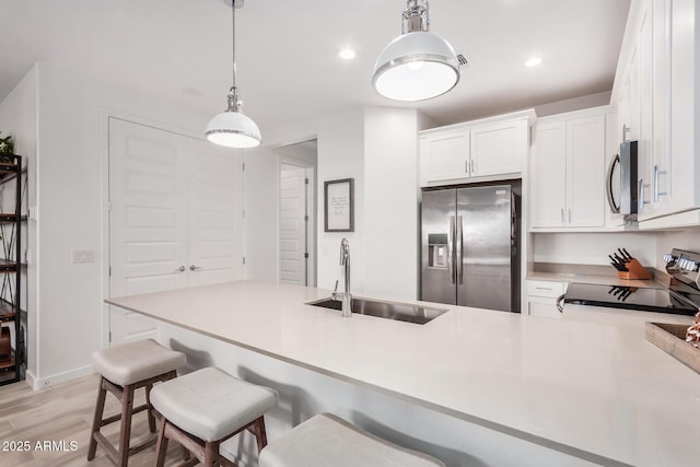 kitchen with kitchen peninsula, stainless steel appliances, sink, decorative light fixtures, and white cabinetry