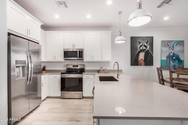 kitchen with sink, stainless steel appliances, kitchen peninsula, decorative light fixtures, and white cabinets