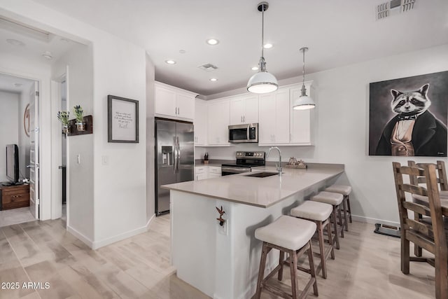 kitchen featuring kitchen peninsula, appliances with stainless steel finishes, sink, decorative light fixtures, and white cabinetry