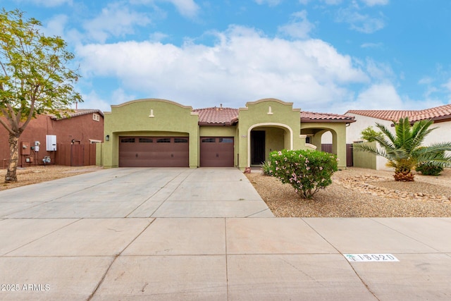 mediterranean / spanish house with a garage, concrete driveway, a tiled roof, fence, and stucco siding