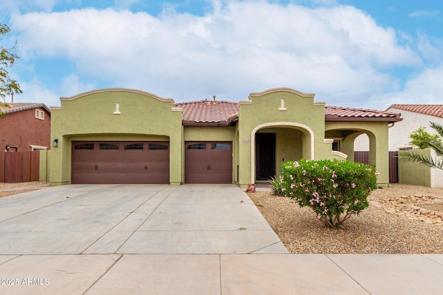 mediterranean / spanish house featuring a garage, fence, a tiled roof, concrete driveway, and stucco siding