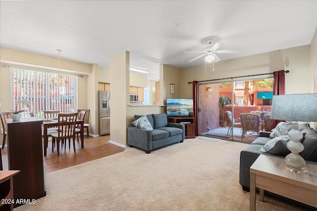 carpeted living room featuring ceiling fan with notable chandelier and a textured ceiling