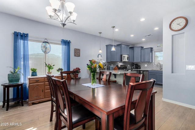 dining area with a notable chandelier, sink, and light hardwood / wood-style flooring