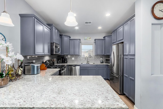 kitchen featuring decorative backsplash, sink, light hardwood / wood-style flooring, hanging light fixtures, and stainless steel appliances