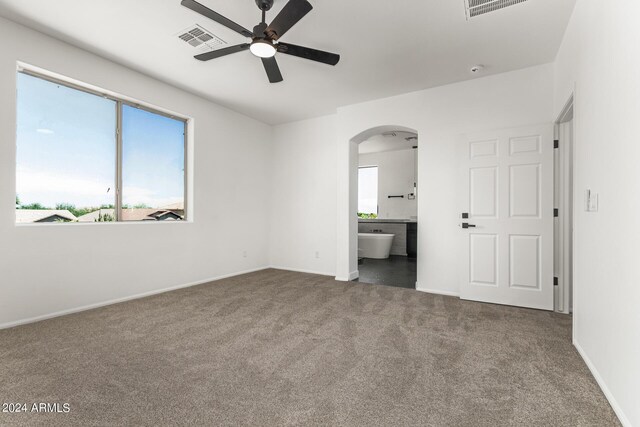 unfurnished bedroom featuring dark carpet, connected bathroom, and ceiling fan