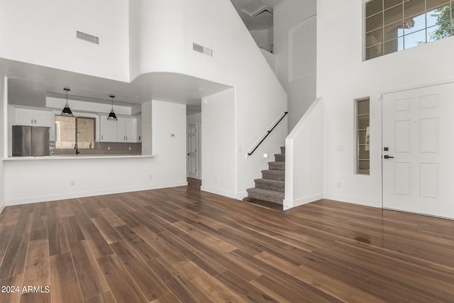 unfurnished living room featuring sink, wood-type flooring, and a high ceiling