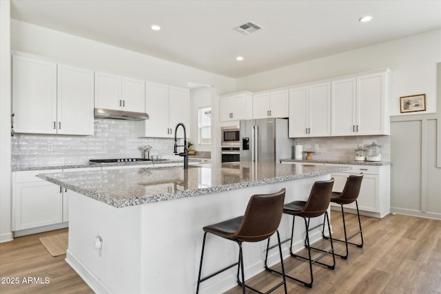 3919 W Abalone Ln, San Tan Valley, AZ 85144 - kitchen featuring under cabinet range hood, stainless steel appliances, white cabinets, decorative backsplash, and an island with sink