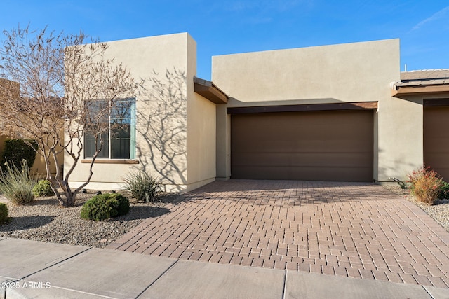 pueblo revival-style home with a garage, decorative driveway, and stucco siding