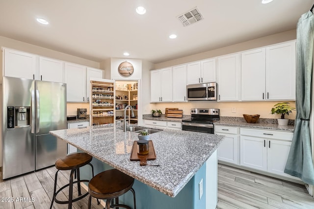 kitchen featuring visible vents, a sink, stone counters, appliances with stainless steel finishes, and a breakfast bar area