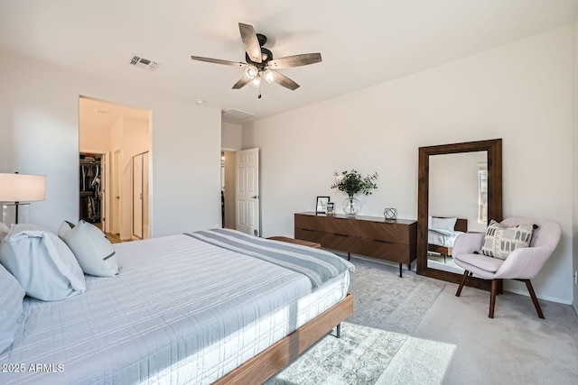 bedroom with a ceiling fan, a closet, a walk in closet, light colored carpet, and visible vents