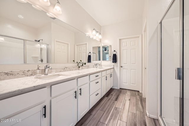 full bath with wood finished floors, a sink, double vanity, and a stall shower