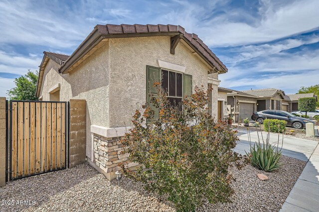 view of side of property featuring a gate, an attached garage, concrete driveway, and stucco siding