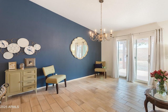 sitting room with lofted ceiling, an accent wall, baseboards, light wood-type flooring, and an inviting chandelier