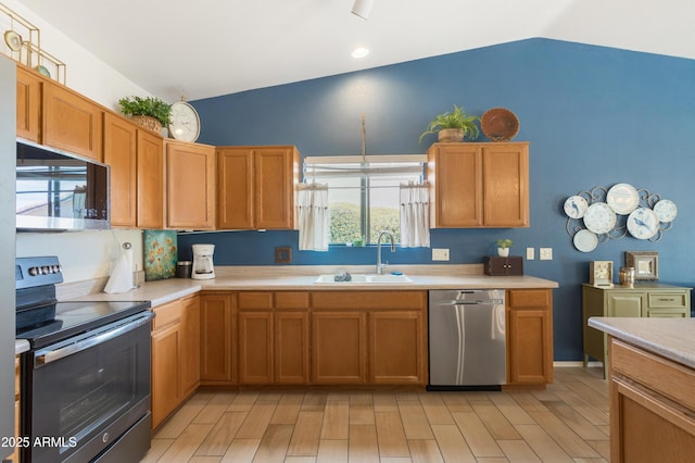 kitchen featuring light wood finished floors, lofted ceiling, appliances with stainless steel finishes, light countertops, and a sink