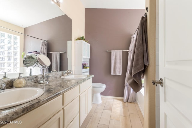 bathroom with baseboards, a sink, toilet, and double vanity