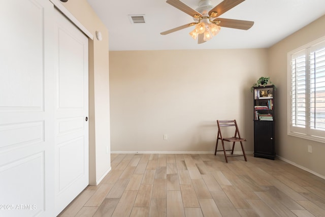 interior space with baseboards, a ceiling fan, visible vents, and light wood-style floors