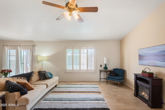 living room with light wood-type flooring, baseboards, a ceiling fan, and a glass covered fireplace