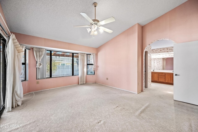 unfurnished bedroom featuring a textured ceiling, ensuite bath, vaulted ceiling, ceiling fan, and light colored carpet