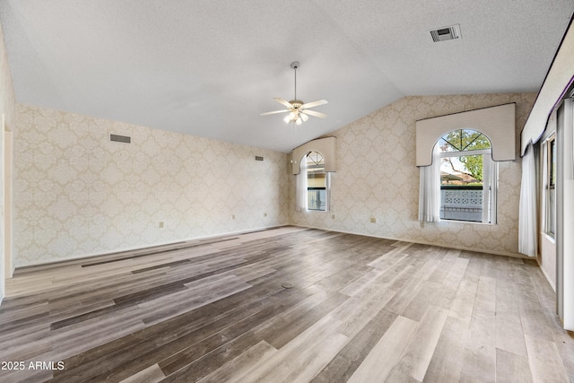 unfurnished living room featuring a textured ceiling, light hardwood / wood-style flooring, vaulted ceiling, and ceiling fan