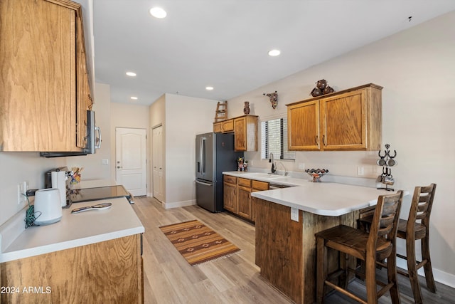 kitchen featuring sink, a kitchen breakfast bar, kitchen peninsula, appliances with stainless steel finishes, and light wood-type flooring