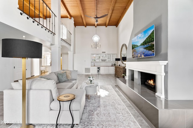 living room featuring beamed ceiling, wooden ceiling, a chandelier, a tile fireplace, and a high ceiling