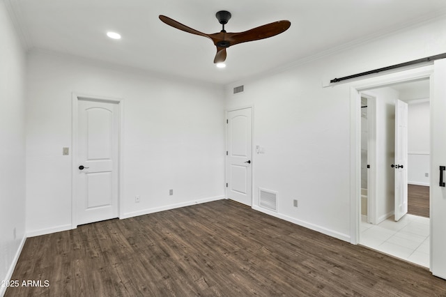 unfurnished bedroom featuring ceiling fan, a barn door, crown molding, and hardwood / wood-style flooring