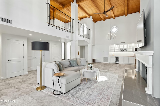 living room featuring a high ceiling, beverage cooler, decorative columns, wooden ceiling, and beam ceiling