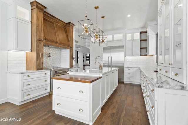 kitchen featuring light stone counters, white cabinetry, a center island with sink, and hanging light fixtures