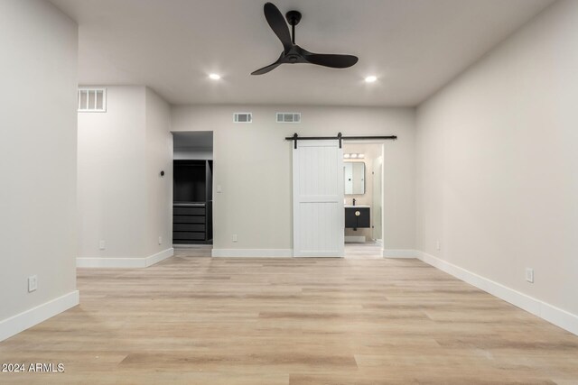 unfurnished bedroom with ceiling fan, a barn door, ensuite bathroom, and light hardwood / wood-style flooring