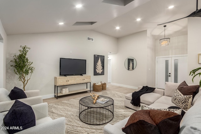 living room featuring light hardwood / wood-style floors, french doors, lofted ceiling, and a notable chandelier