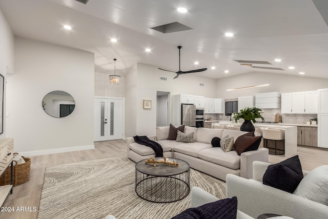 living room with high vaulted ceiling, ceiling fan with notable chandelier, and light wood-type flooring