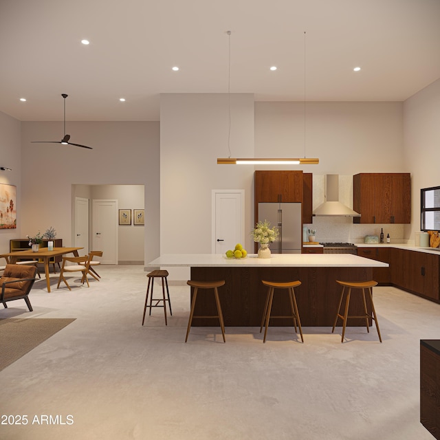 kitchen featuring wall chimney range hood, a towering ceiling, high end refrigerator, and a kitchen breakfast bar