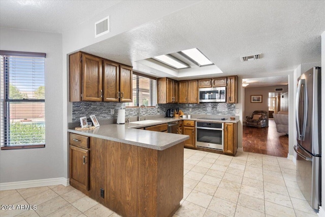 kitchen featuring appliances with stainless steel finishes, visible vents, brown cabinets, and a peninsula