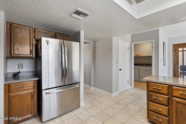 kitchen featuring visible vents, brown cabinetry, washing machine and clothes dryer, and freestanding refrigerator